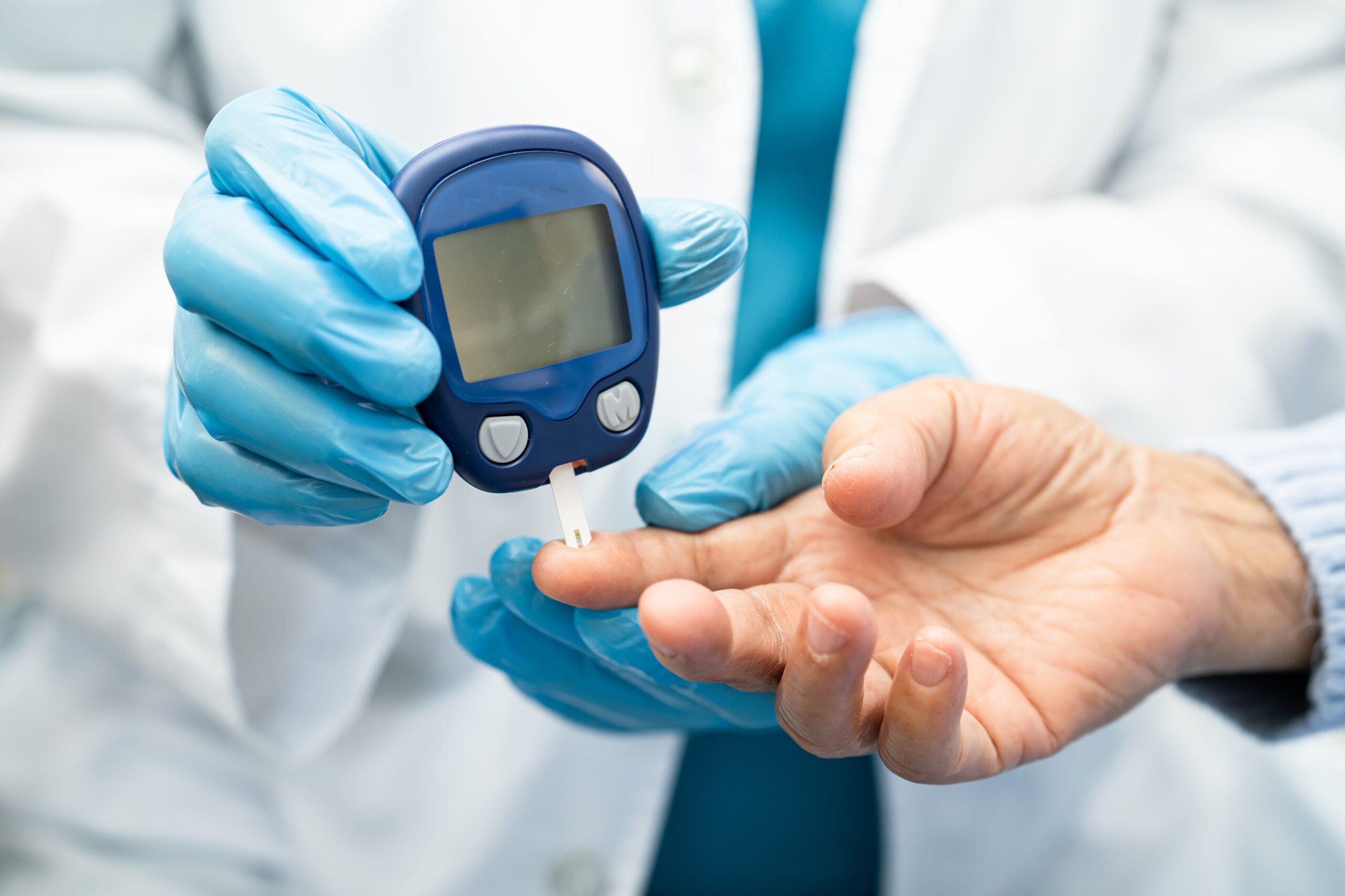 Close-up of doctor in blue medical gloves taking a blood sample from a Diabetes patient's finger-tip.