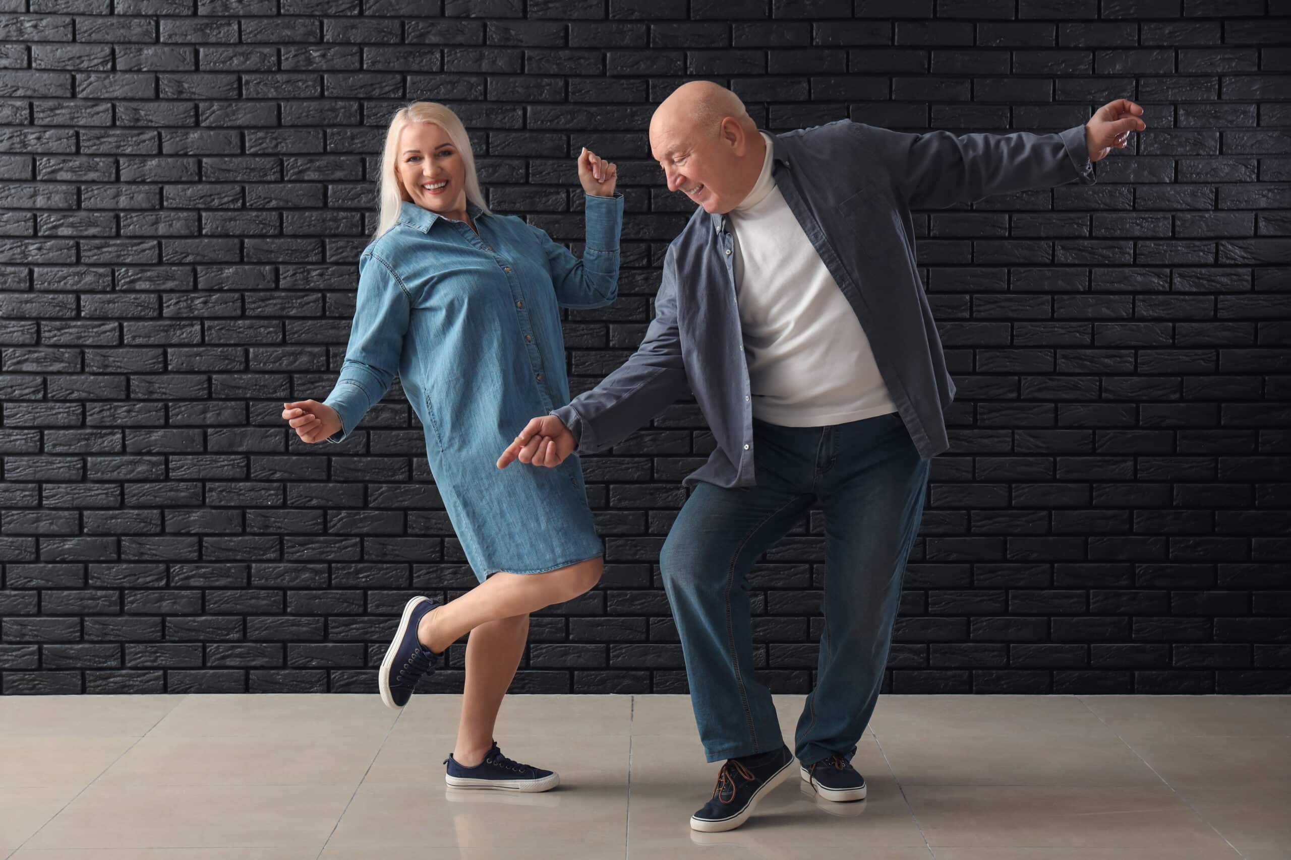 Senior couple smiles while dancing together in comfortable clothing and shoes.