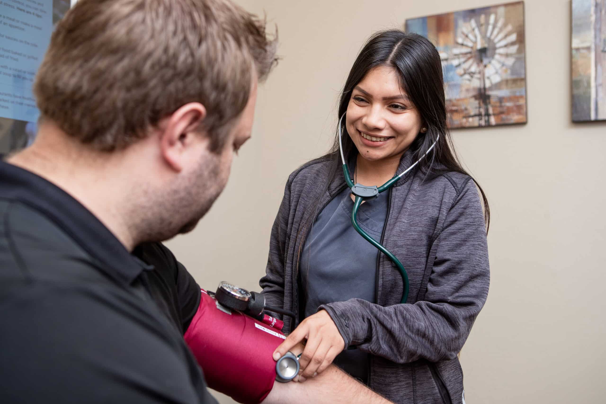Doctor takes blood pressure of her patient while smiling at him as he looks down at the gauge.