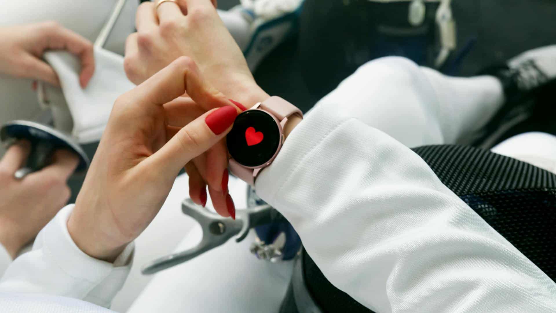 Close-up of woman's hands looking at a smartwatch with a red heart in the middle monitoring health.