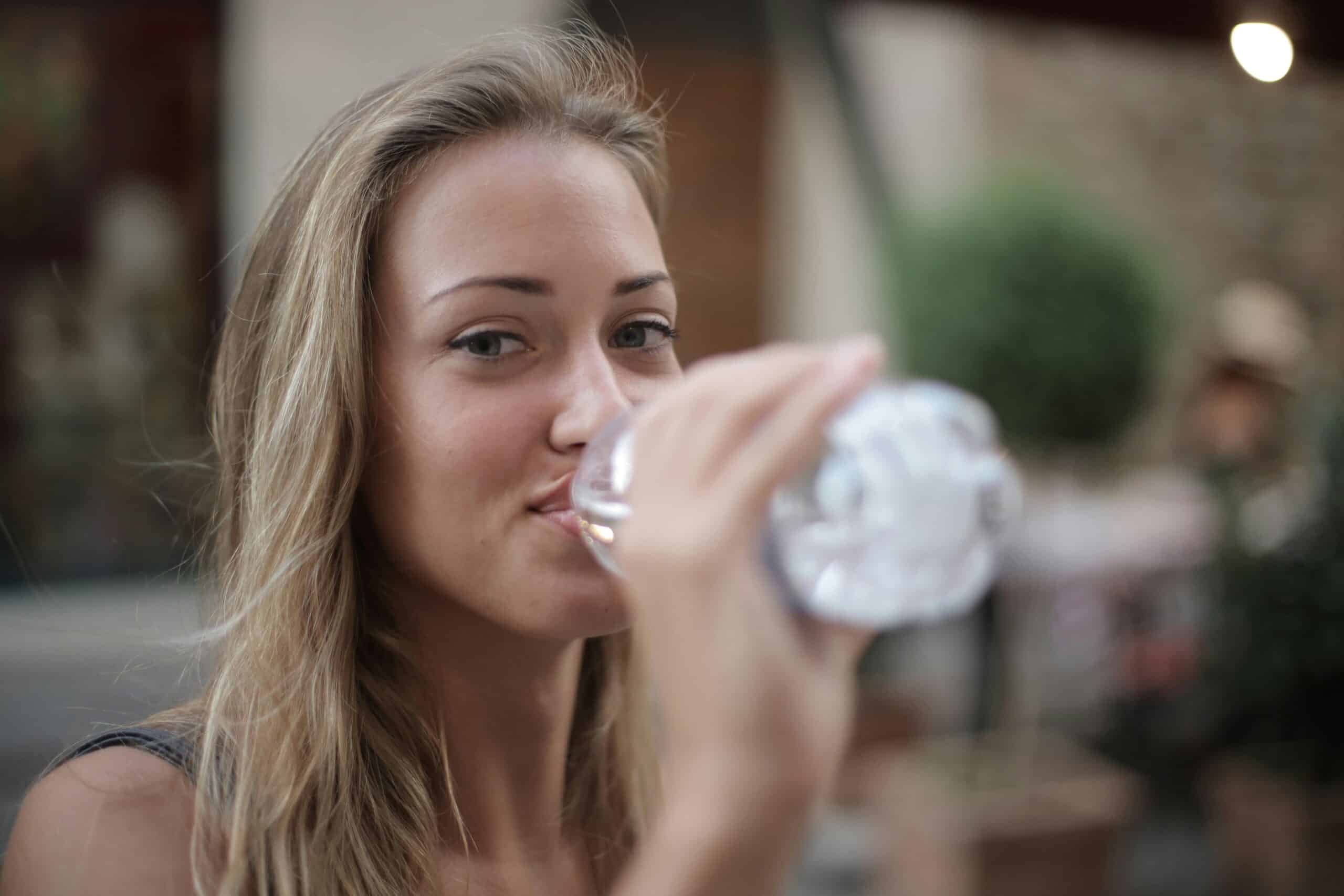 A healthy woman with blond hair drinks from a clear water bottle to stay hydrated.