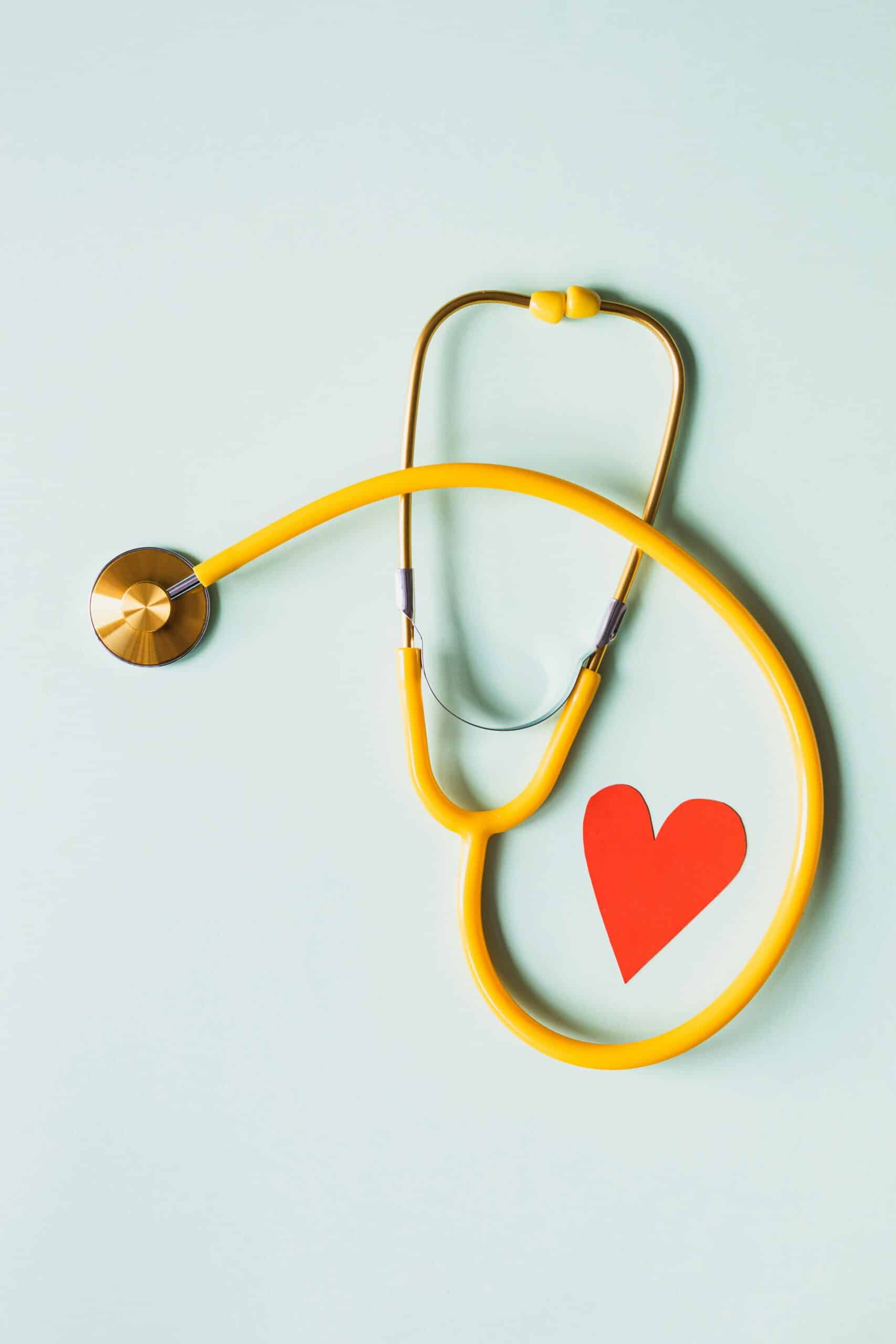 A yellow stethoscope with bronze metal circles around a red paper heart to indicate heart health.