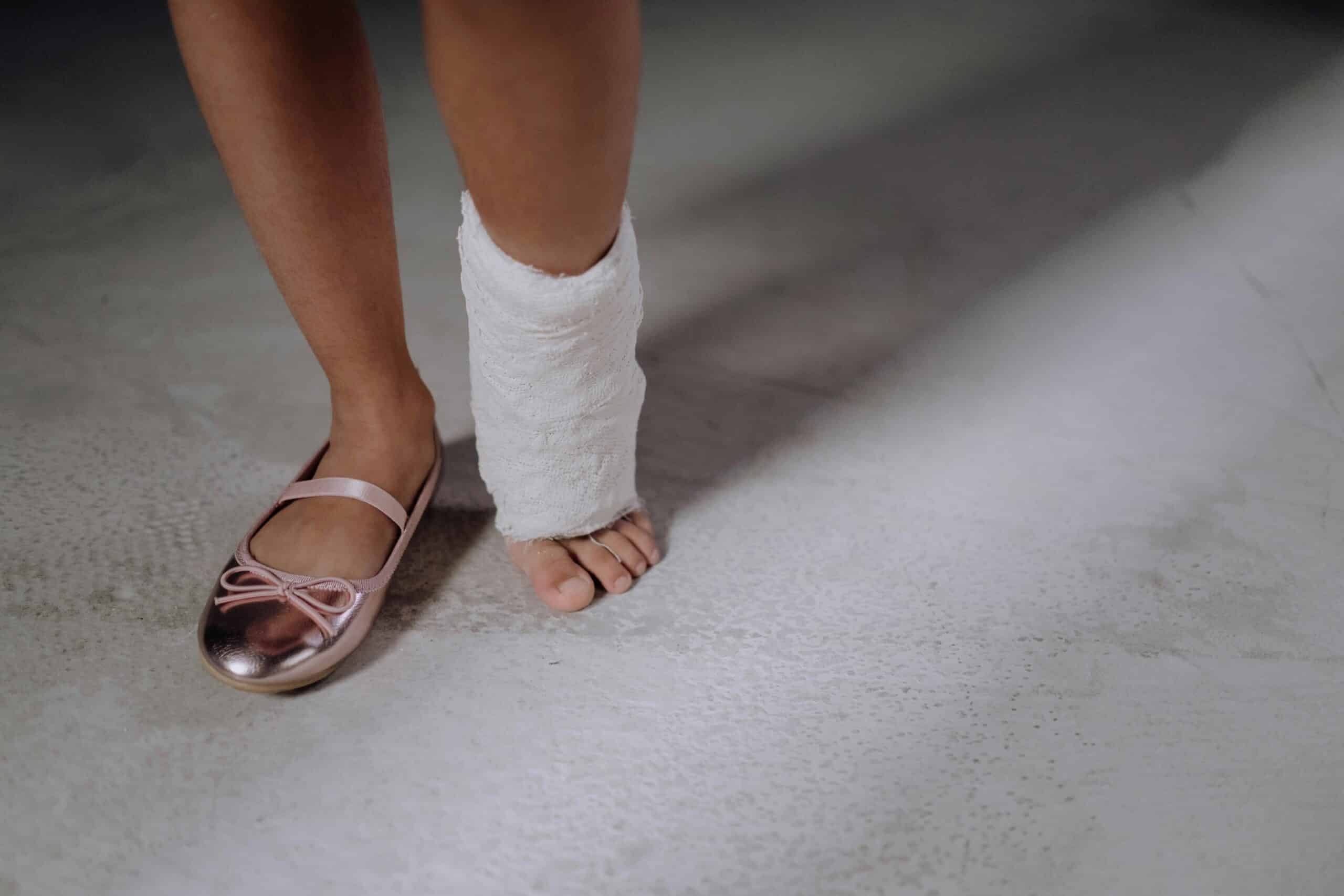 A female ballet dancer's feet, one with a slipper and the other wrapped in bandaging from ankle swelling.