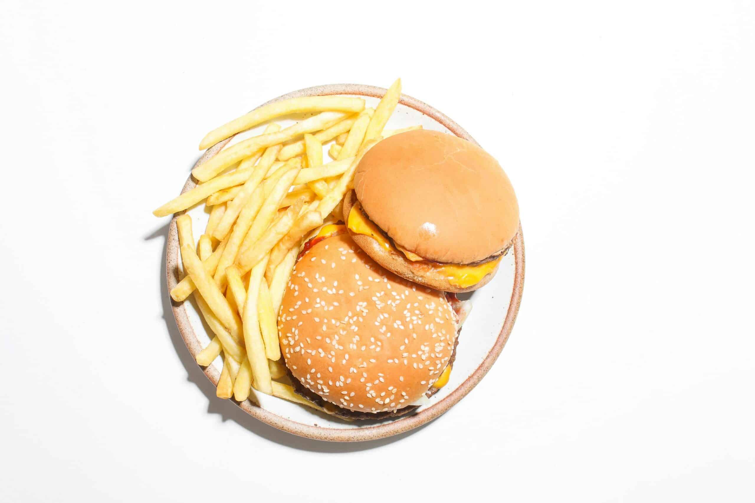 Two cheeseburgers and french fries sit on a white plate as indicators of high cholesterol.